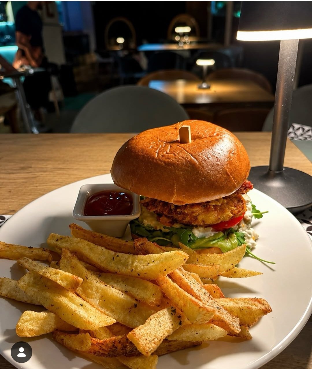 Gourmet burger with crispy exterior served on white plate alongside golden french fries and ketchup
