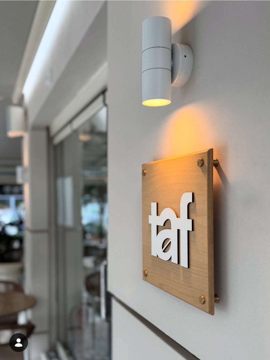 Modern wall-mounted wooden sign with white eft lettering, illuminated by a cylindrical wall sconce light fixture in a contemporary interior hallway