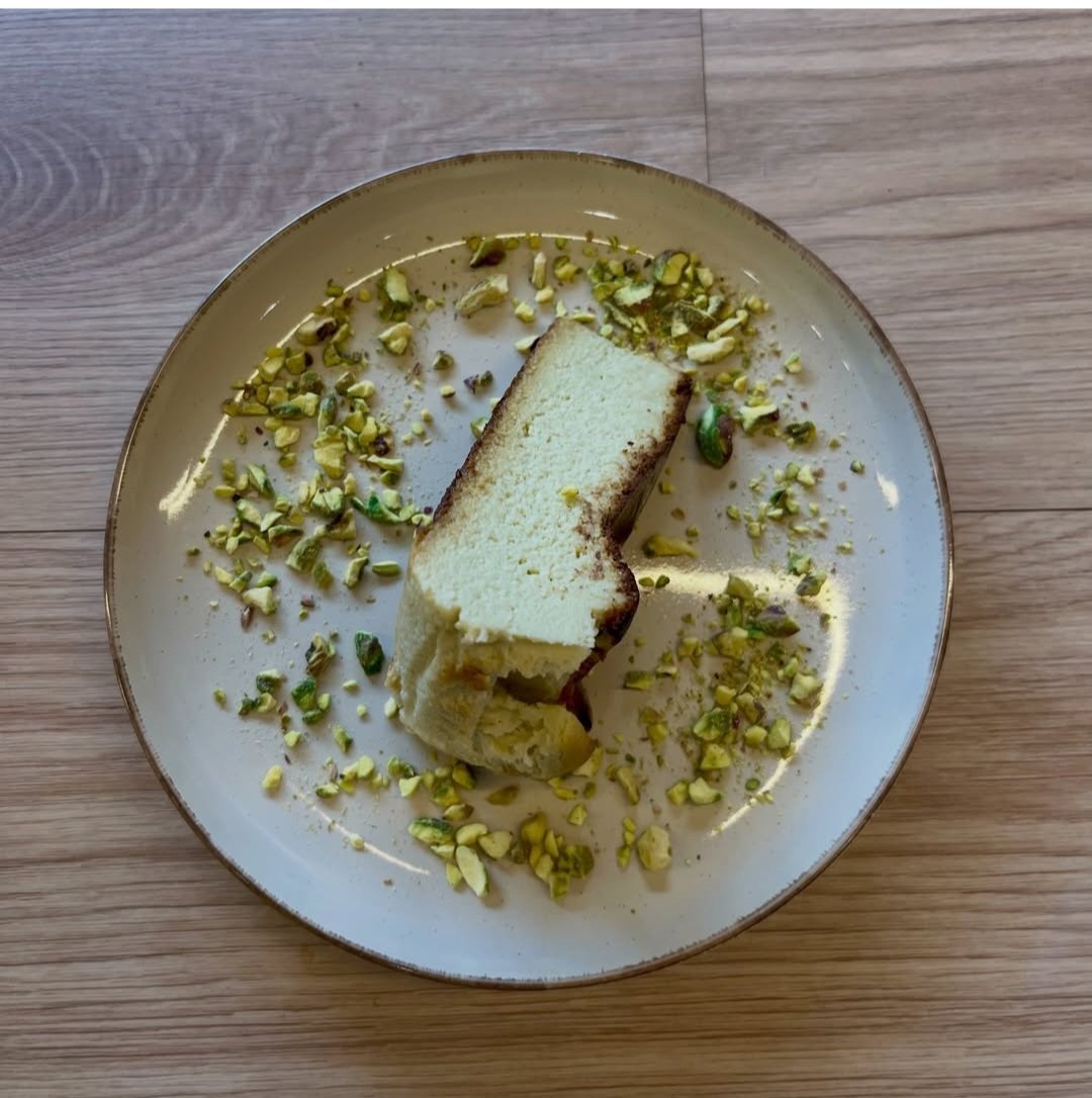 A white plate with sliced pound cake topped with crushed pistachios and a dusting of powdered sugar on a wooden surface