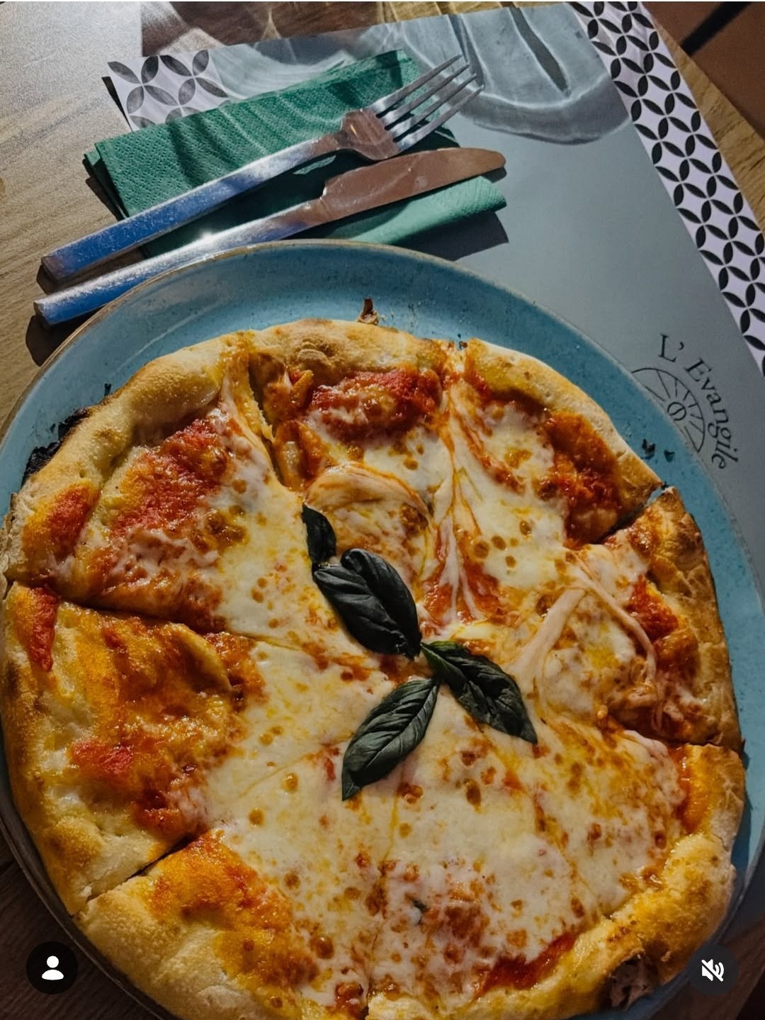Margherita pizza on a blue plate with fresh basil leaves, served with cutlery and napkins on a wooden table