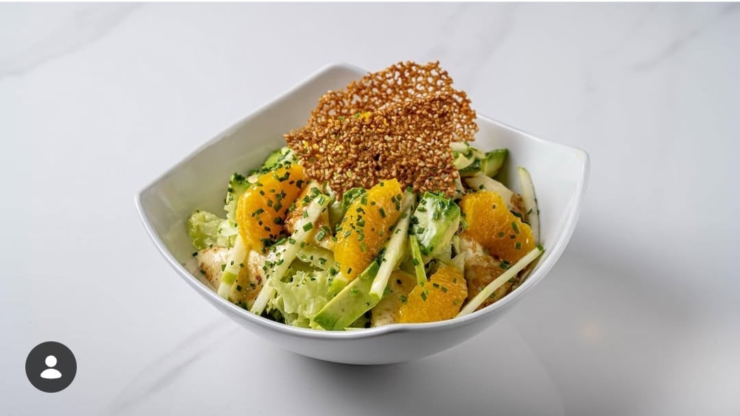 White bowl with mixed vegetables including avocado, orange squash, and herbs topped with sesame seeds