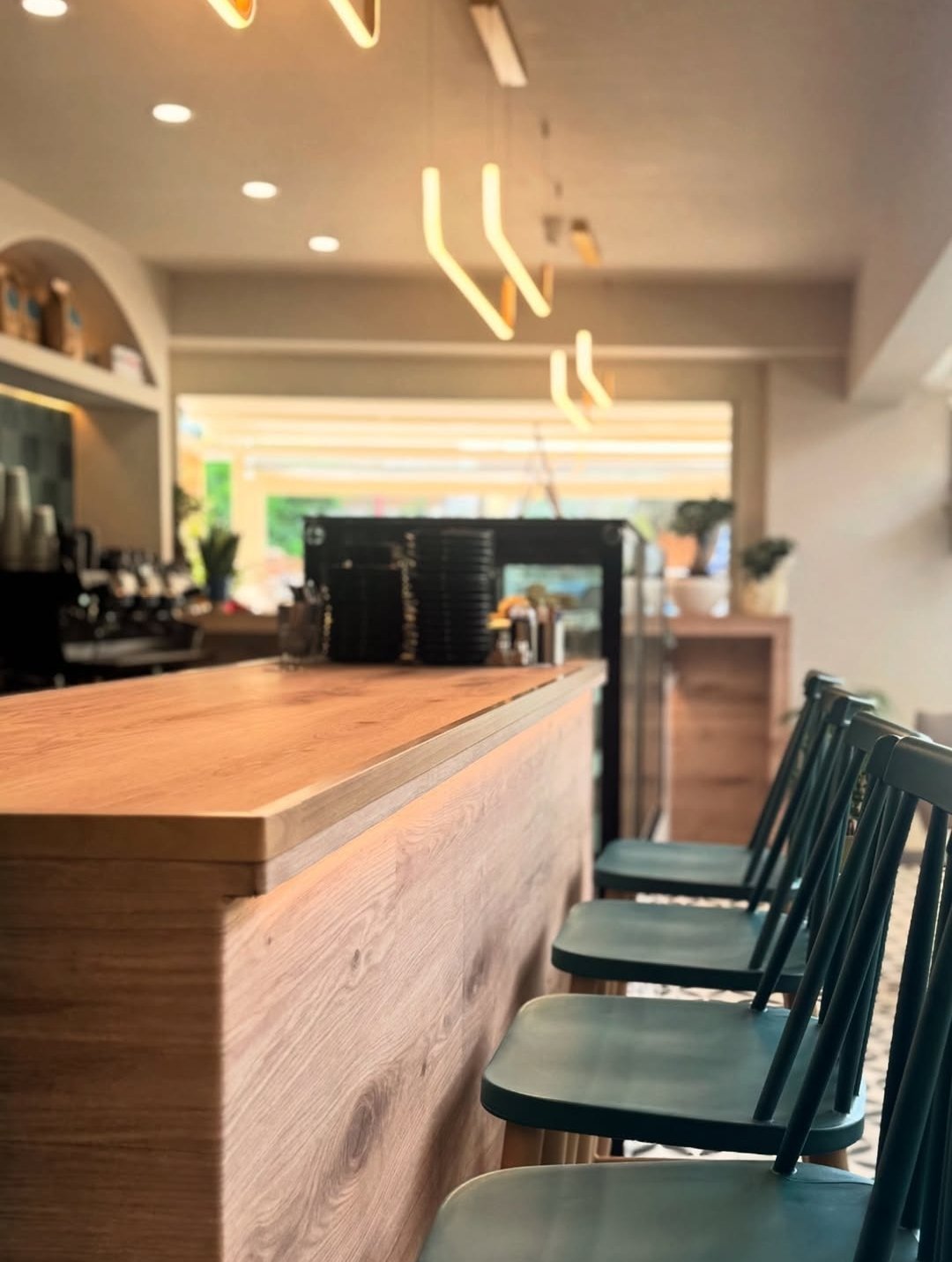 Modern cafe interior with wooden counter, black bar stools, neon signs, and recessed ceiling lights
