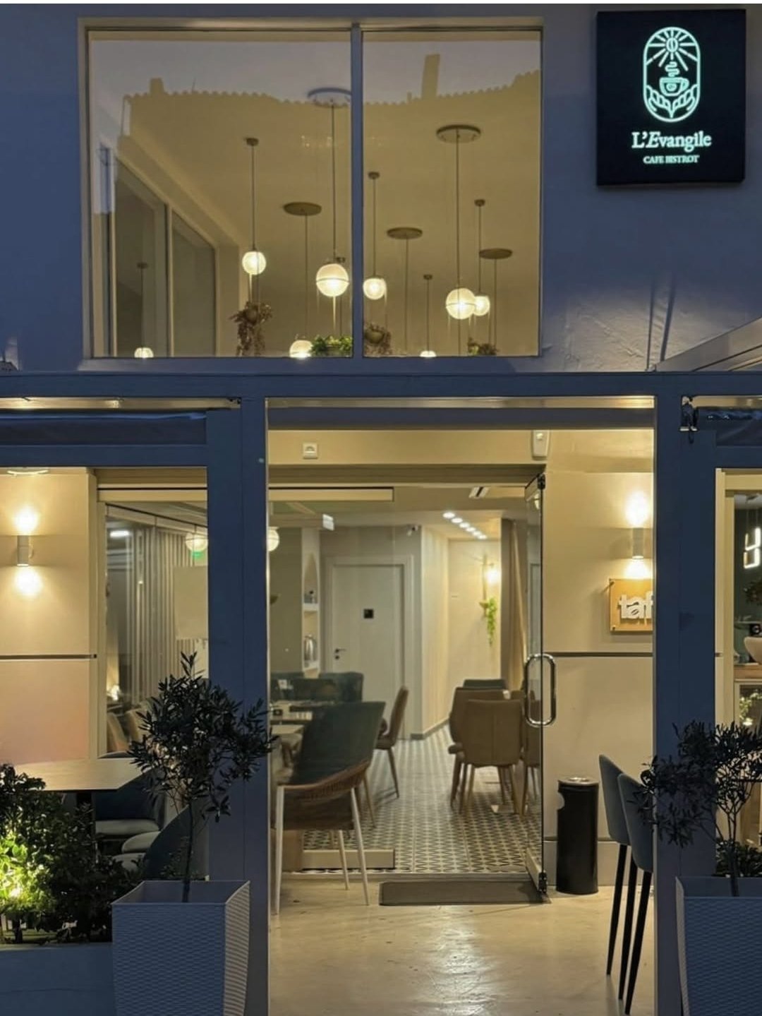 Modern storefront with blue facade, glass doors and windows, pendant lights, and L'Evangile cafe bistrot sign at night